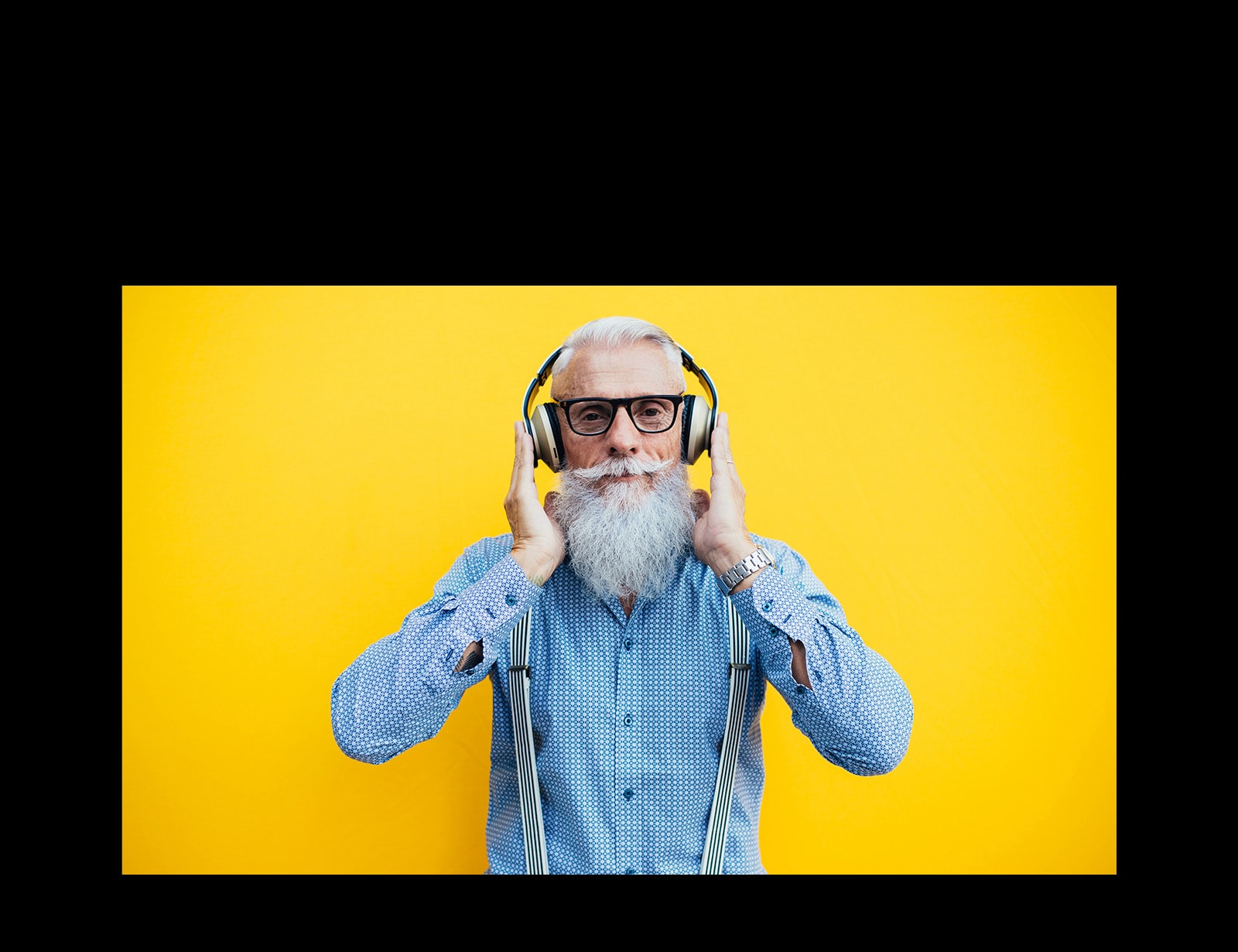Starý otec s náhlavnou súpravou stojí pred žltou stenou.