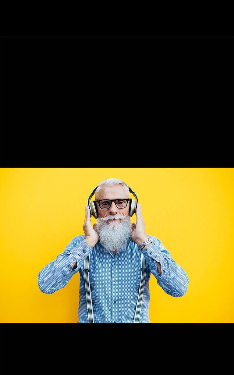 Starý otec s náhlavnou súpravou stojí pred žltou stenou.