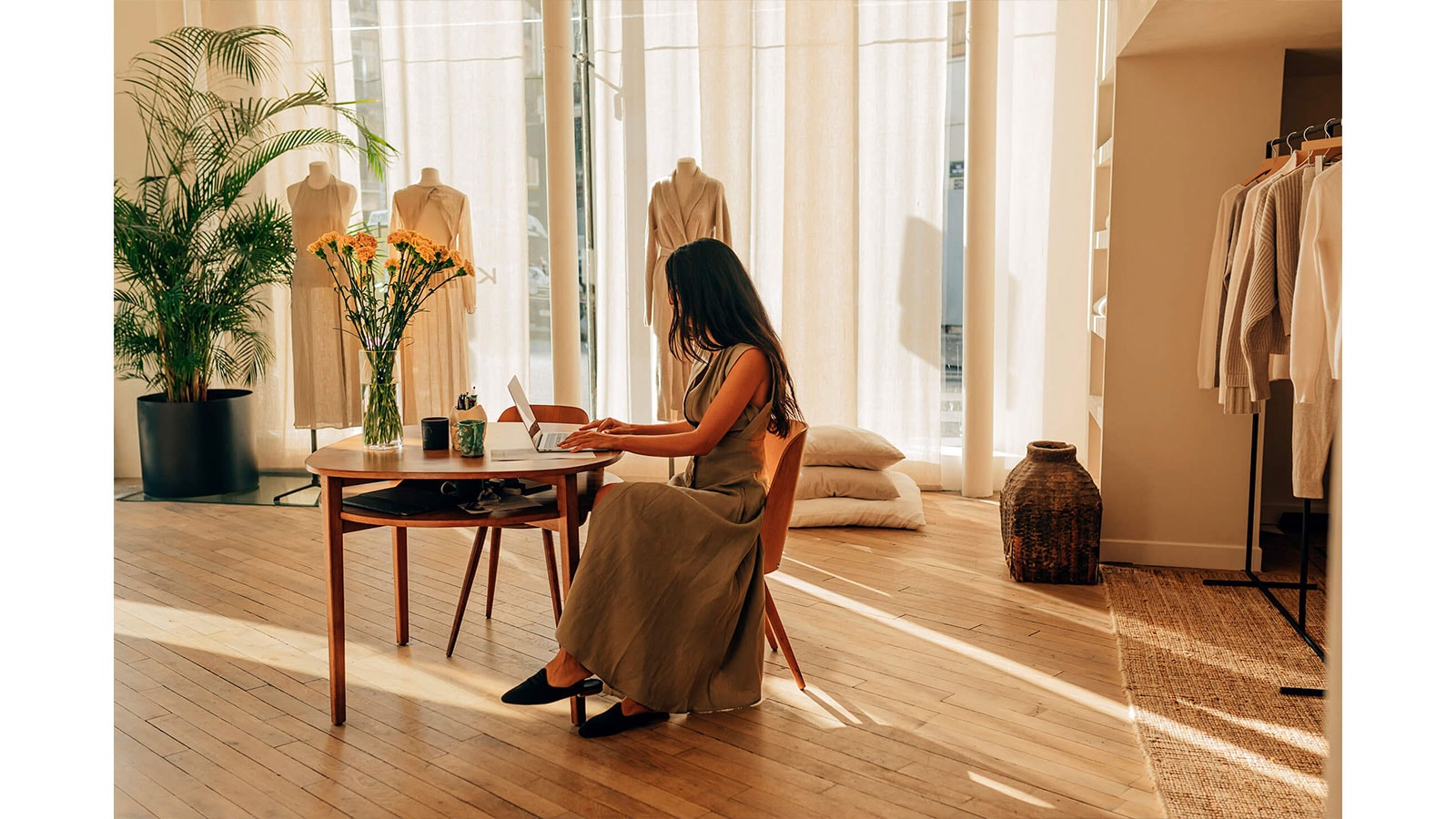 Obraz dizajnérky Le Kasha sediacej za stolom v jemne osvetlenom štúdiu. 