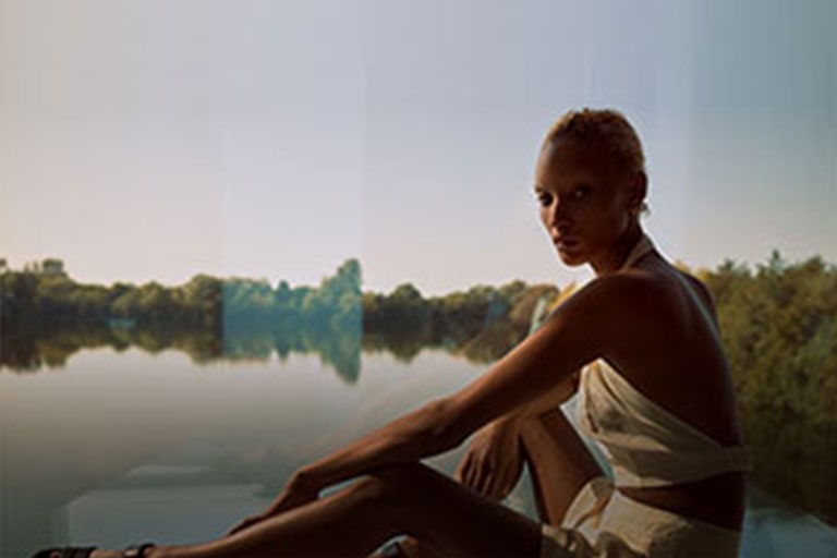 Obrázok modelky v jednom z kúskov z minimalistickej kolekcie Winter Sun sediacej pred krásnym jazerom