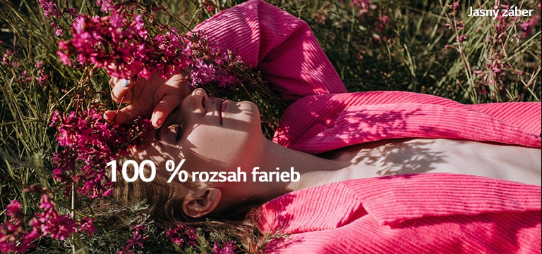 Video zobrazuje mladé dievča, ktoré si drží ruku pred očami a leží na trávnatej lúke s ružovými kvetmi. Počas prehrávania videa naberajú farby na sýtosti a percentuálny indikátor rozsahu farieb za zvyšuje zo 70 % na 100 %.