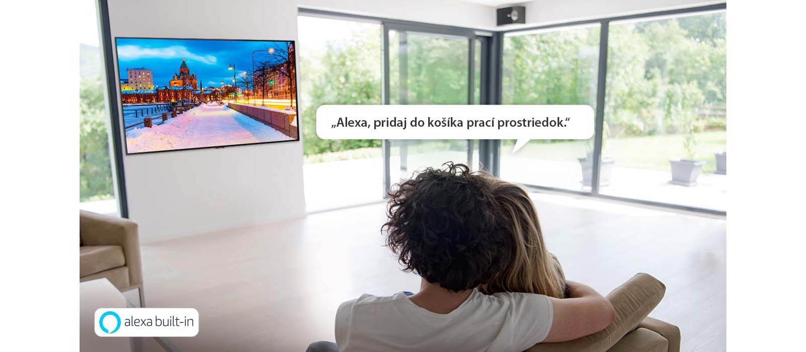 Muž so ženou sedia na gauči a používajú službu Alexa od spoločnosti Amazon na pridanie pracieho prostriedku do košíka