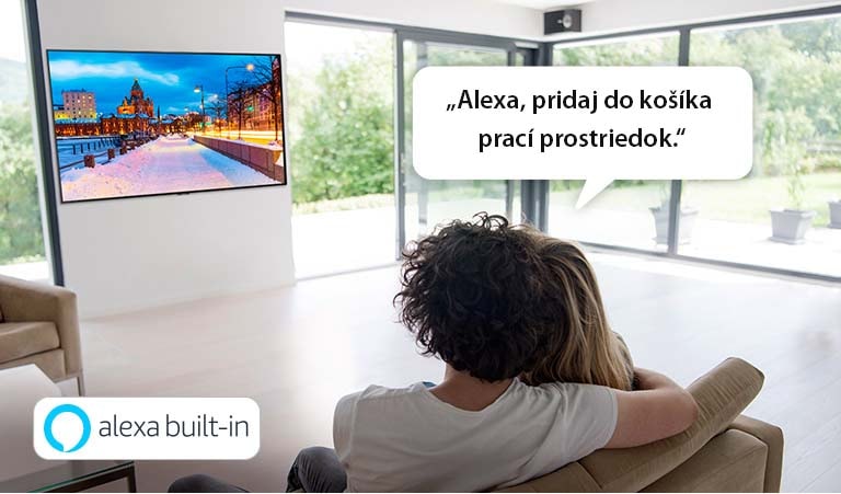 Muž so ženou sedia na gauči a používajú službu Alexa od spoločnosti Amazon na pridanie pracieho prostriedku do košíka