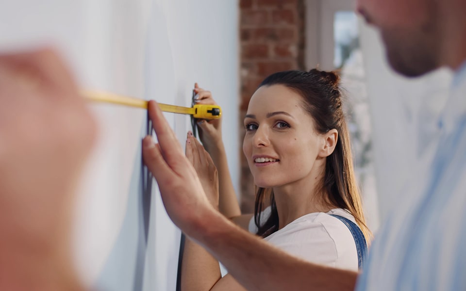 A couple measuring the space on the wall where they will install the LG TV.