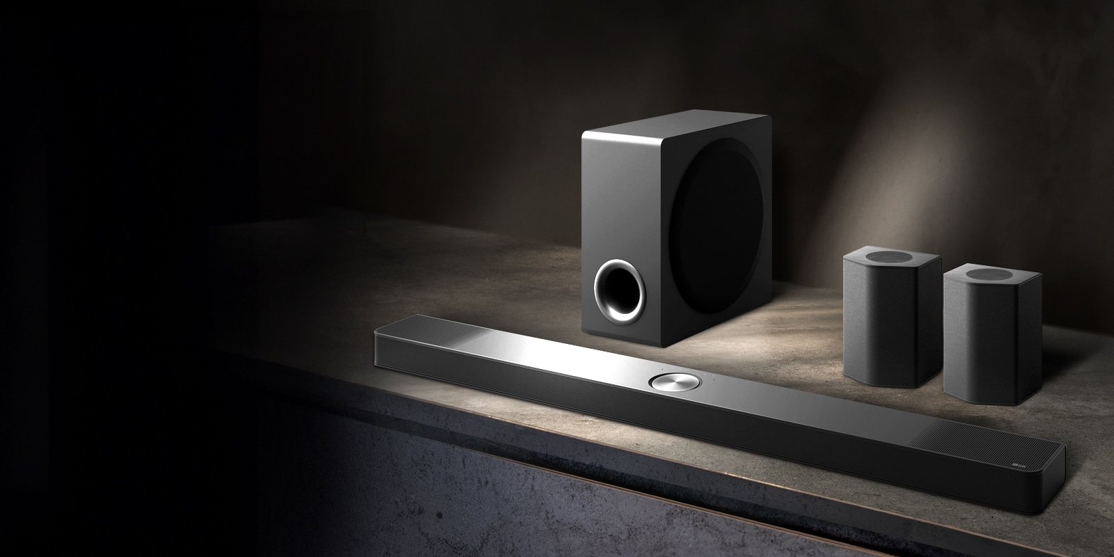 LG Soundbar, zadné reproduktory a subwoofer sú umiestnené v šikmej perspektíve na hnedej drevenej polici v čiernej miestnosti, obklopené tmou, pričom svetlo dopadá len na zvukový systém.
