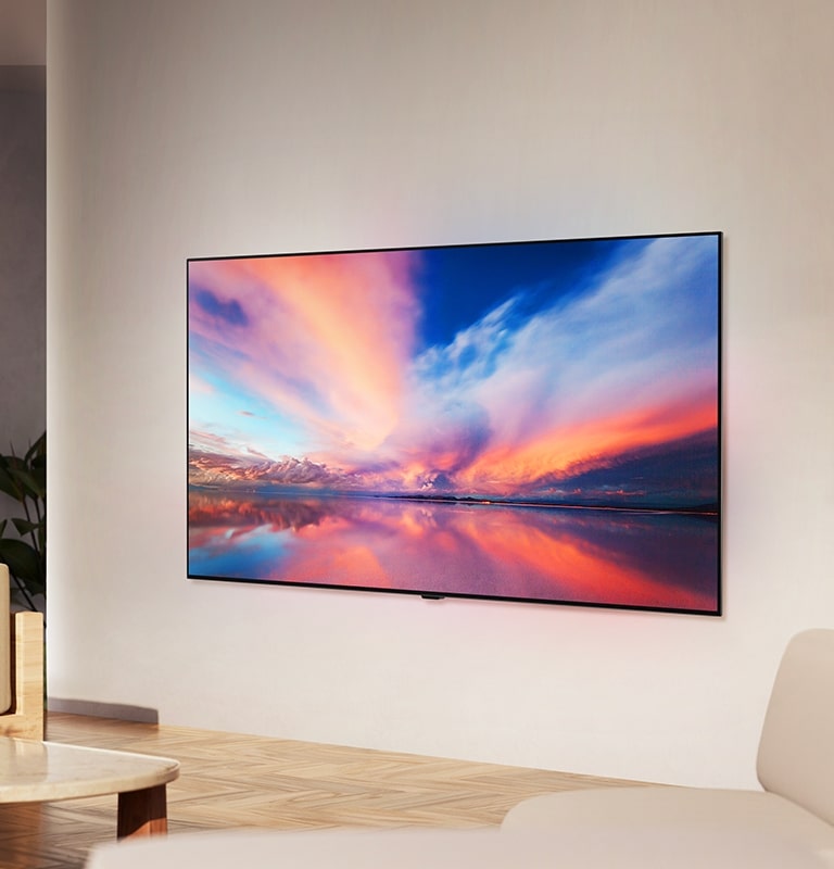 LG OLED TV, OLED B4 sur le mur d'un espace de vie neutre montrant une photo colorée d'un coucher de soleil sur l'océan. 