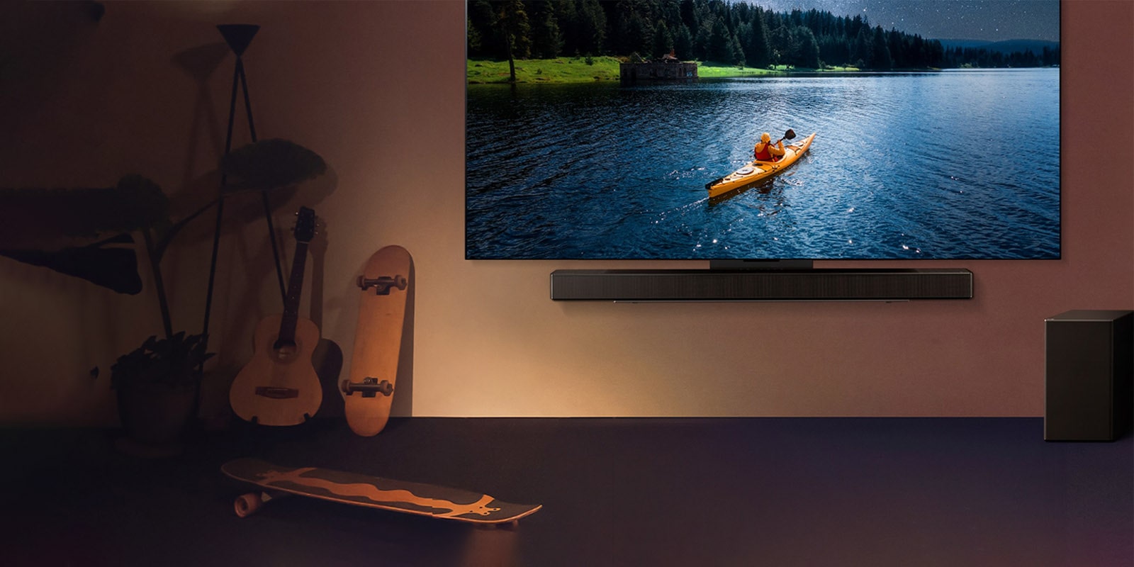 Un téléviseur et une barre de son LG montés sur un mur et un caisson de basses au sol à droite. Le téléviseur montre une personne en kayak sur un lac et des ombres douces cascadent sur le mur.