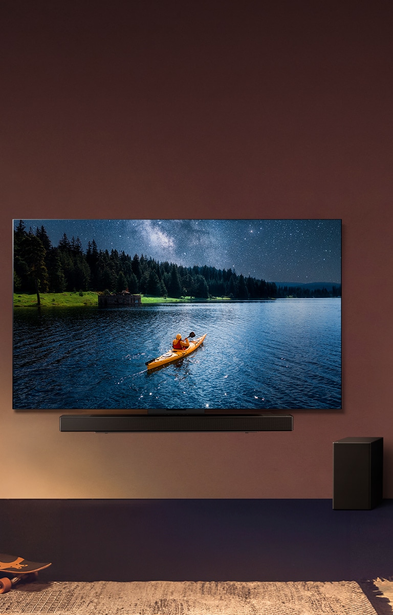 Un téléviseur et une barre de son LG montés sur un mur et un caisson de basses au sol à droite. Le téléviseur montre une personne en kayak sur un lac et des ombres douces cascadent sur le mur.