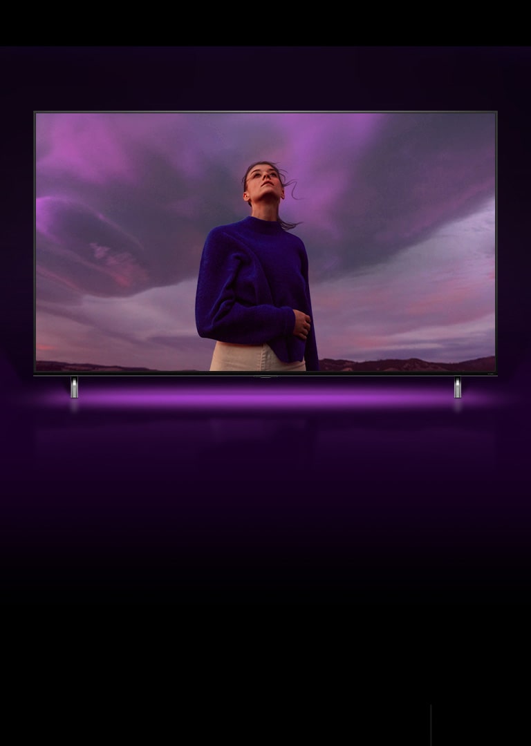 Une femme se tient debout et regarde un ciel violet et l’image effectue un zoom arrière pour montrer la même femme sur l’écran du téléviseur QNED.