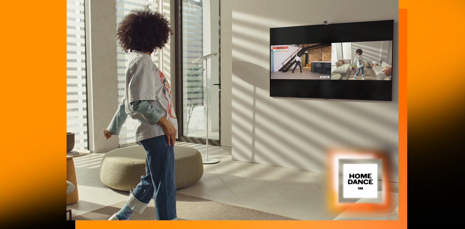 Une femme se tient debout au milieu du salon, danse et regarde la télévision en même temps. Le téléviseur montre une scène de didacticiel de danse sur la gauche et reflète une femme qui danse sur le côté droit de l’image. Le logo « 1million home dance » est visible dans le coin inférieur droit.
