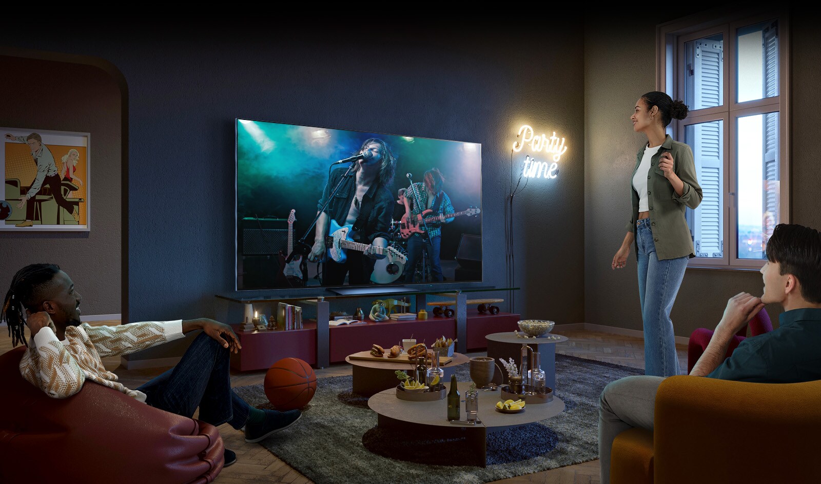 Un concert est diffusé sur l’écran de la télévision, deux hommes sont assis sur le canapé et le pouf. Une femme est debout et profite du concert. Du pop-corn, des nachos et du coca sont posés sur la table au milieu des amis.