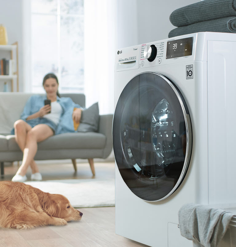 Une vue de côté du lave-linge posé sur un côté, et de l’autre côté un chien et une femme au téléphone.