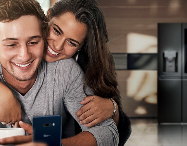 Un couple regarde un smartphone dans la cuisine avec un grand sourire.