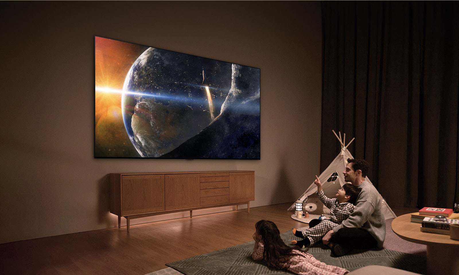 一家人坐在光線昏暗的客廳地板上，旁邊是一張小桌子，大家抬頭看著牆上安裝的 LG TV，電視螢幕上顯示著太空中的地球。