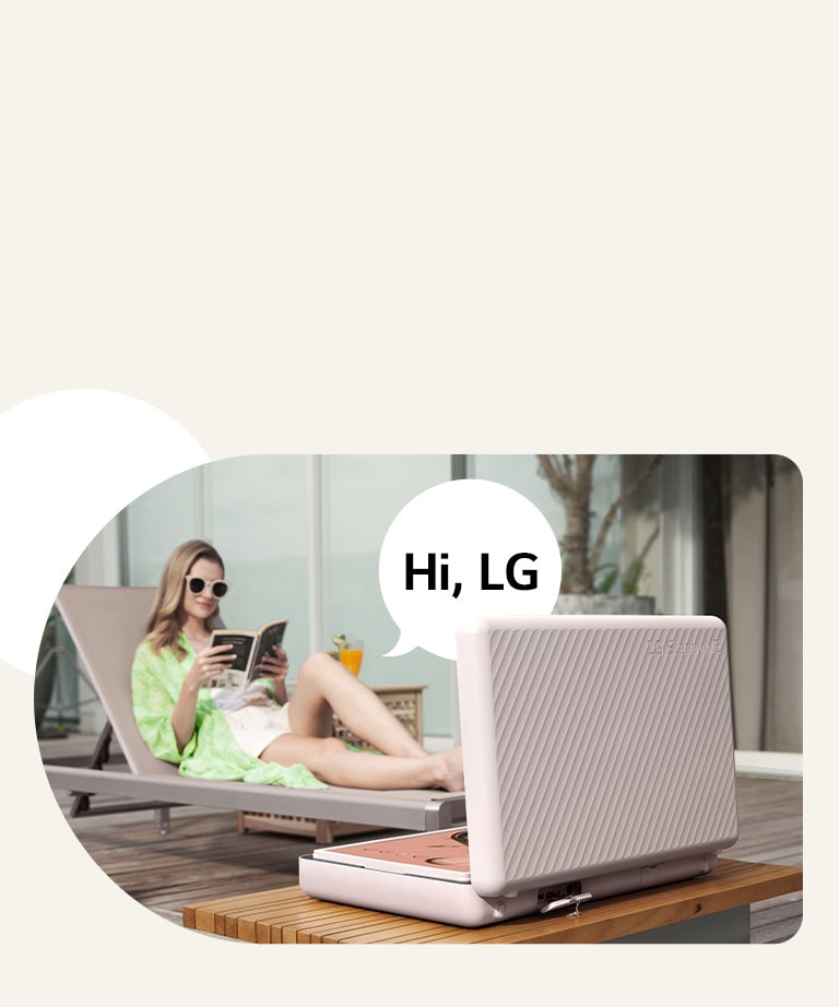 LG StanbyME閨蜜機 Go 後視圖，放在露臺桌正前方。女人在海灘椅上徹底放鬆，使用語音控制螢幕。為了闡述此場景，她的右側顯示帶有「嗨，LG」文字的說話氣泡。