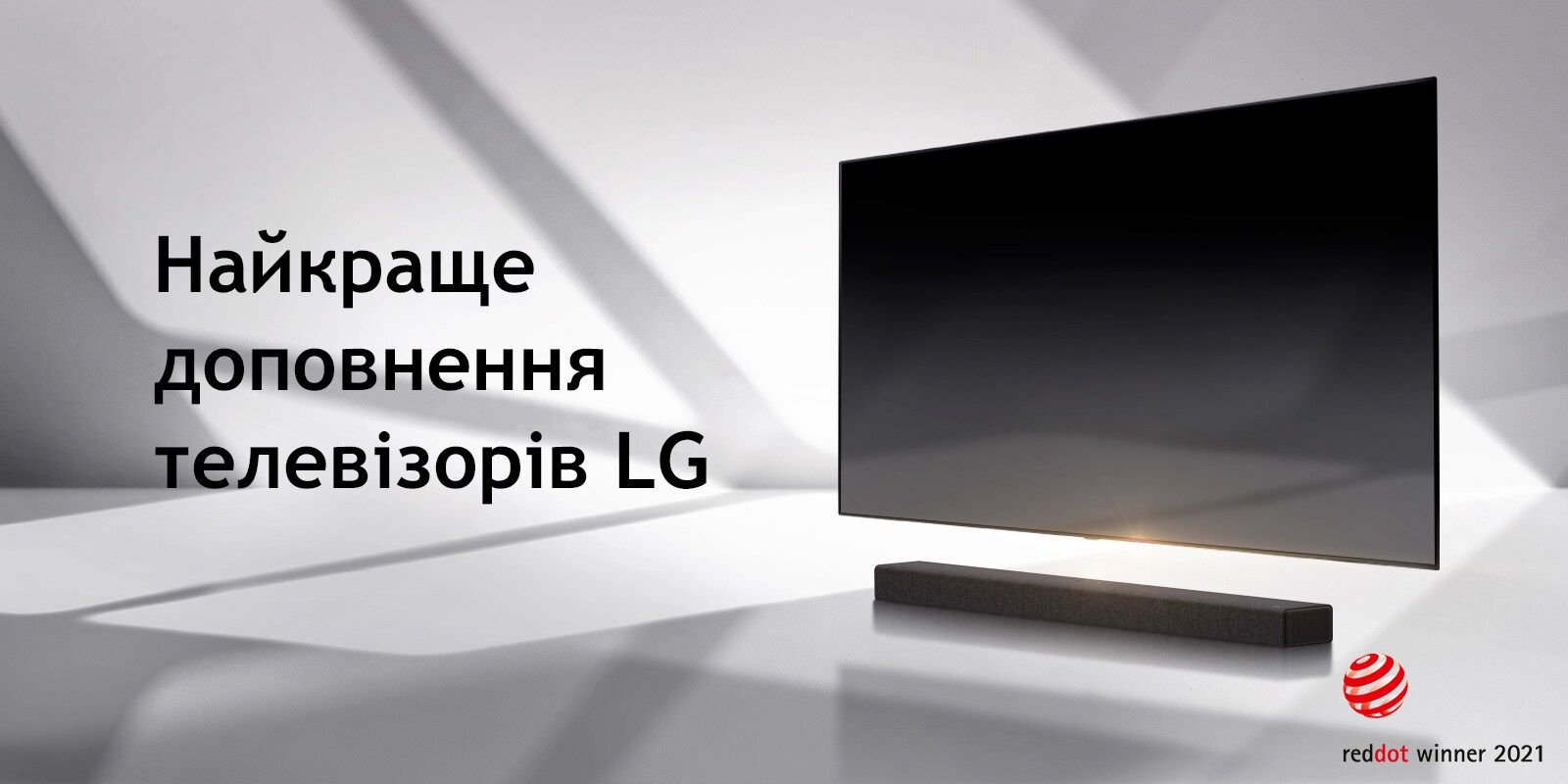 Саундбар і телевізор розташовано на підлозі білого кольору, а ззовні праворуч падає тінь.