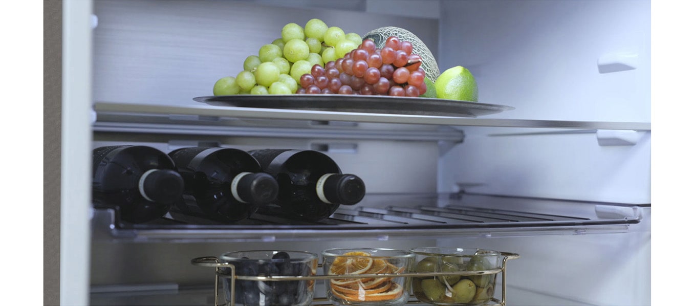 Зображено холодильник з нижньої морозильною камерою LG з фруктами на верхній полиці, пляшки вина посередині та ще більше фруктів на нижній полиці.