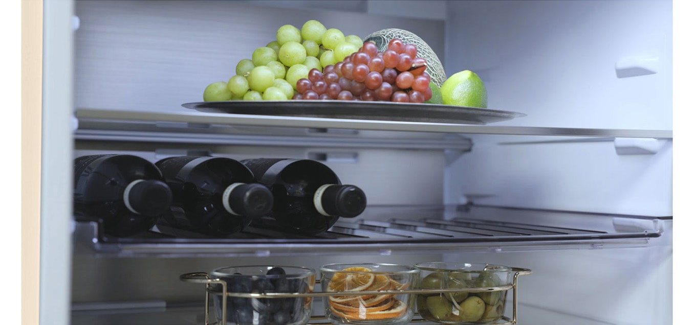 Зображено холодильник з нижньої морозильною камерою LG з фруктами на верхній полиці, пляшки вина посередині та ще більше фруктів на нижній полиці.