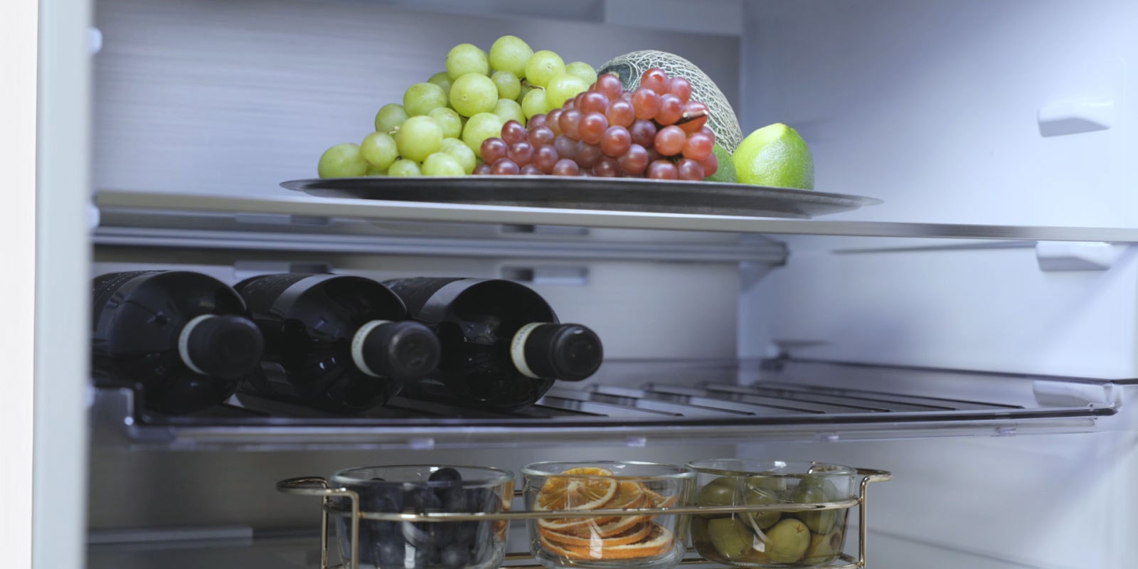 Зображено холодильник з нижньої морозильною камерою LG з фруктами на верхній полиці, пляшки вина посередині та ще більше фруктів на нижній полиці.