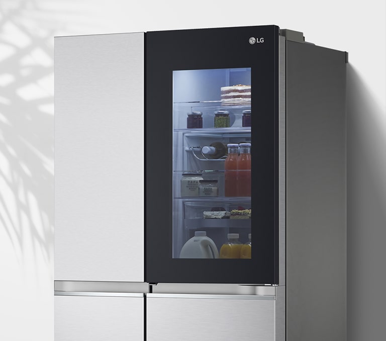 Показано холодильник біля стіни з підсвіченим віконцем у дверцятах, що дозволяє побачити вміст всередині на полицях.