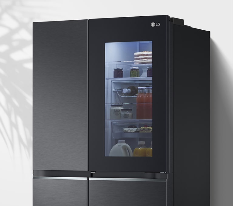 Показано холодильник біля стіни з підсвіченим віконцем у дверцятах, що дозволяє побачити вміст всередині на полицях.