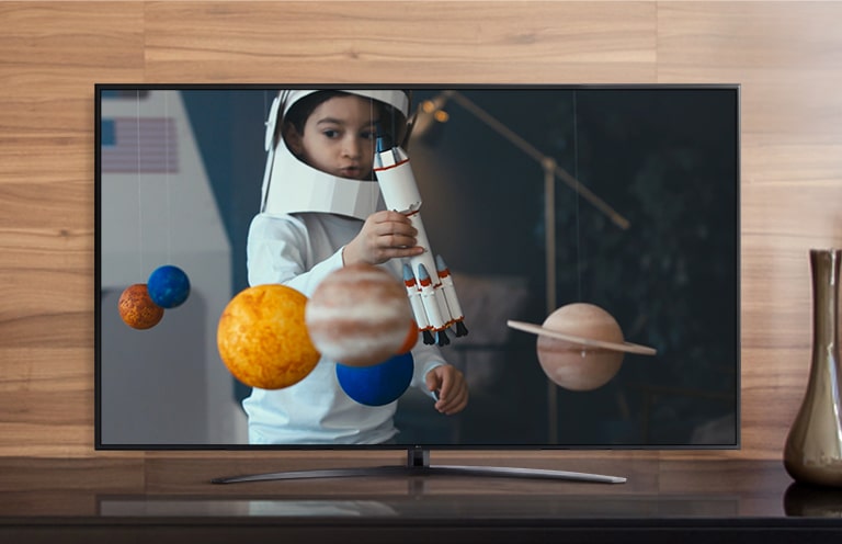 На екрані телевізора відтворюється відео з хлопчиком, одягнутим у саморобний скафандр космонавта, який грається з космічним кораблем у своїй кімнаті, прикрашеній мініатюрами планет (відтворення відео)