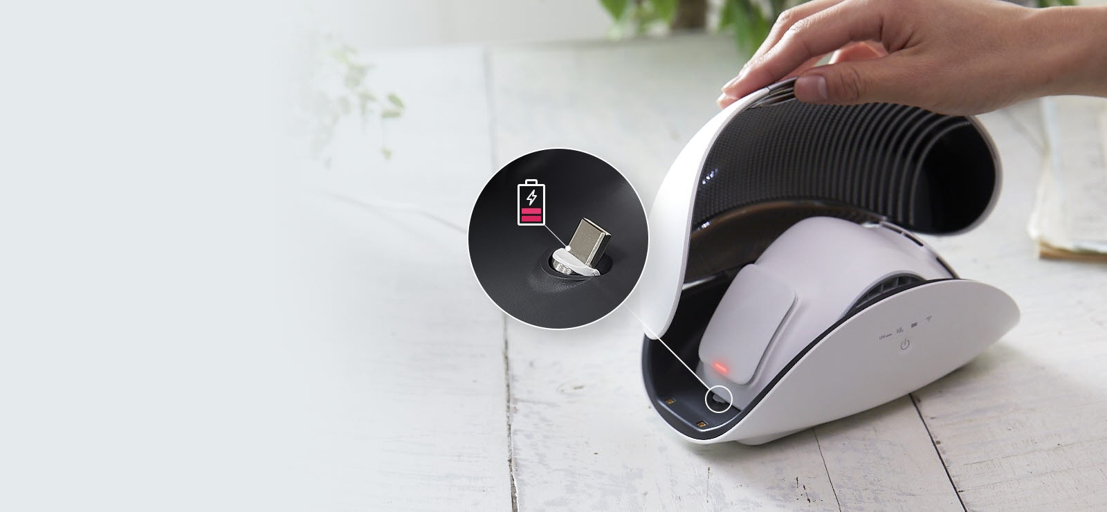 Рука тримає відкриту кришку кейсу для очисника повітря індивідуального використання PuriCare™ так, щоб зручно показати власне очисник всередині. Збоку від очисника повітря індивідуального використання PuriCare™ - червоне світло, а вставне зображення по колу з лінією збоку від маски показує збільшений вигляд місця для заряджання маски. Також є значок батареї, червоного кольору, що означає, що заряд майже порожній, що вказує на те, що пора підключити його до мережі.