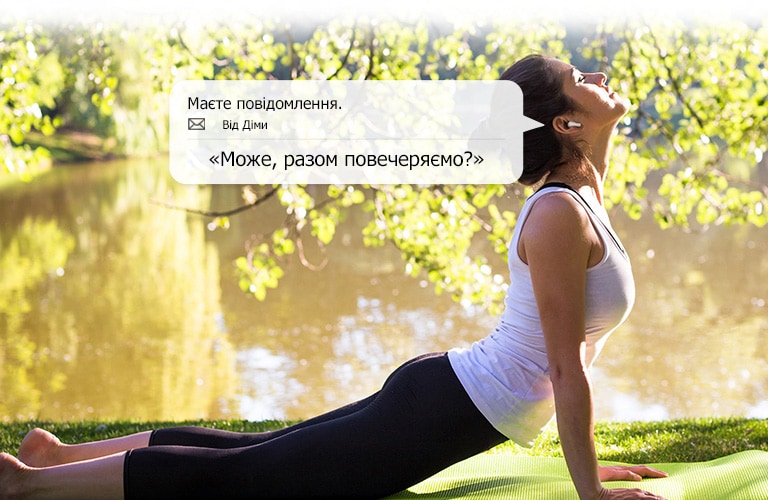 Жінка виконує вправи з розтягування, нахиляючись, щоб торкнутися землі, та водночас прослуховує повідомлення, які їй зачитують навушники.