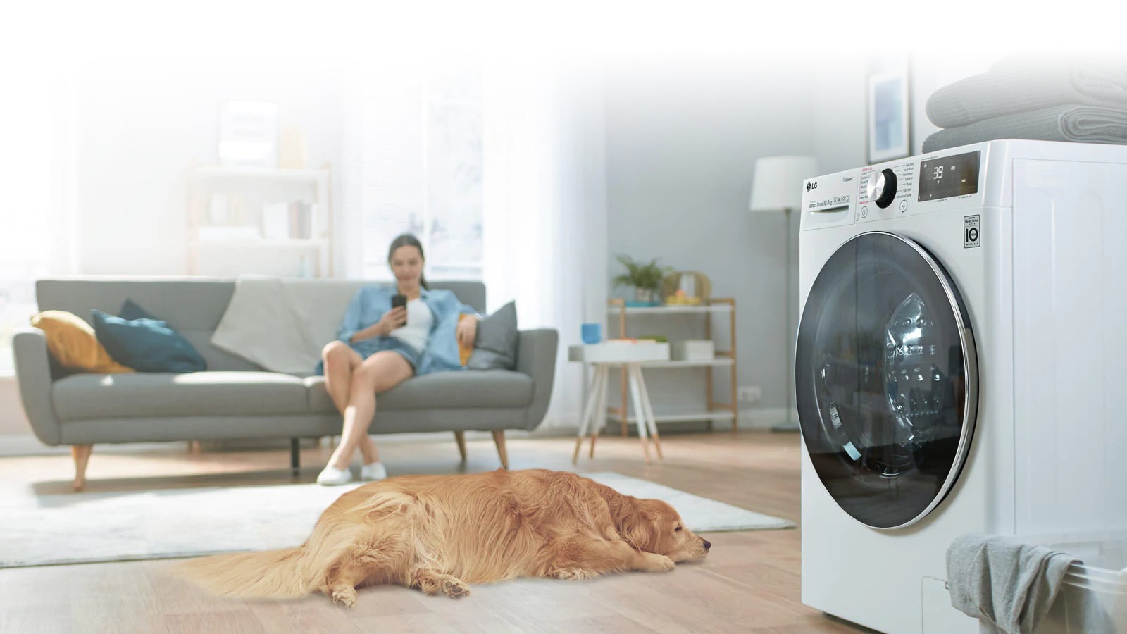 Вид збоку пральної машини, біля якої з одного боку перебуває собака, а з іншого — жінка, яка розмовляє телефоном.
