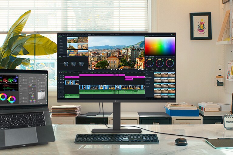 Творчий робочий простір із монітором LG та підключеним ноутбуком, на яких відображається інтерфейс редагування відео з інструментами корекції кольору та часовою шкалою.