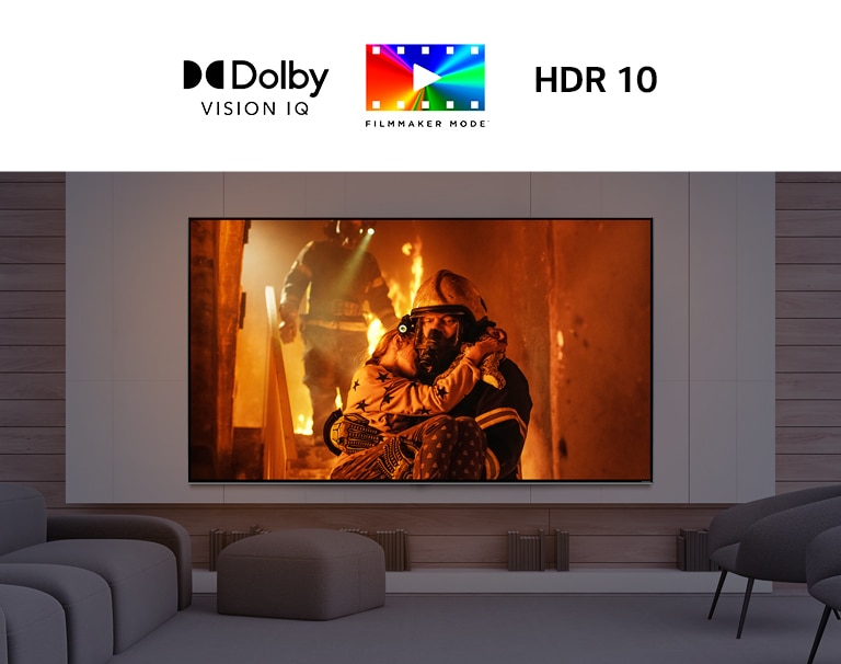 Телевізор із великим екраном на стіні перед низькими кріслами. На екрані показано людину, яка виносить дитину з пожежі.