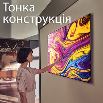 Жінка дивиться на телевізор, який висить на стіні й відтворює витвір мистецтва.