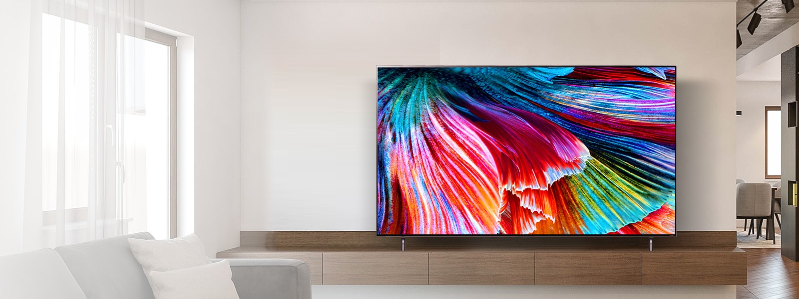QNED MiniLED TV stood on a wooden cabinet against a light wall in a light modern interior. The screen shows a close-up image of multi-colored petals billowing.