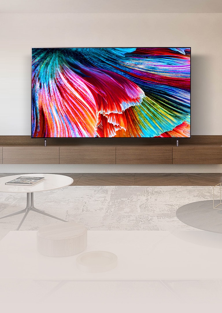QNED MiniLED TV stood on a wooden cabinet against a light wall in a light modern interior. The screen shows a close-up image of multi-colored petals billowing.