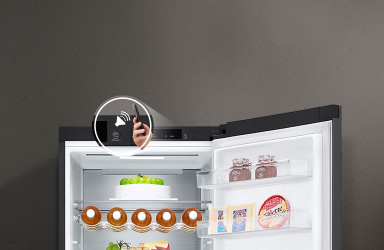 Зображено справа на передньому плану руку, що тримає смартфон, на якому видно інтерфейс моніторингу енергоспоживання в застосунку ThinQ. Позаду зображено інтер'єр кухні з холодильником ліворуч з підсвіченим віконцем InstaView Door-in-Door.
