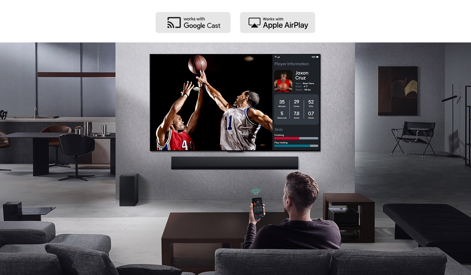 Person in their living room holding their phone. On the phone is a transmitting icon showing that the phone screen is being mirrored on the TV. On the TV is a basketball game to the side is the mirrored screen, showing player statistics. 