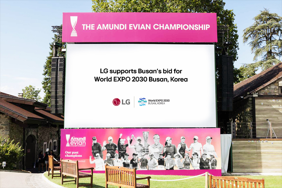 A large pink billboard in a park setting promoting the Amundi Evian Championship and LG's support for Busan's World EXPO 2030 bid.
