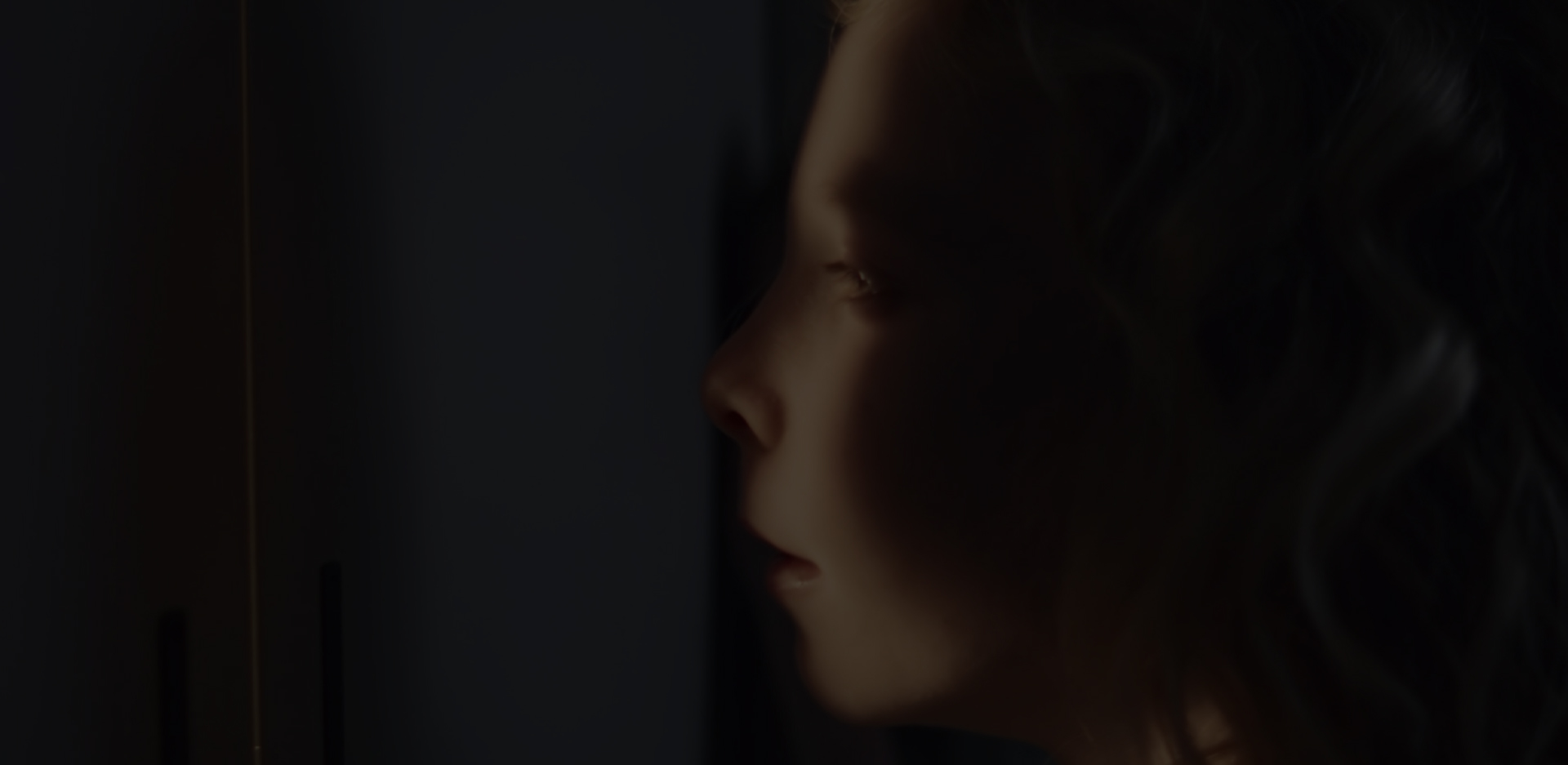 A close-up shot of a girls face, partially in shadow, partially illuminated as she peers out from a hiding place.