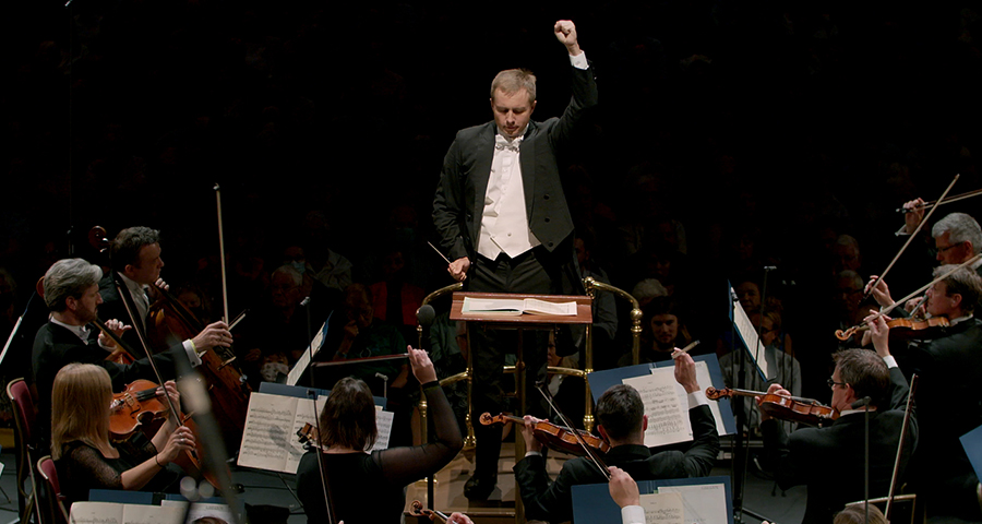A conductor directs an orchestra, his hand raised in the air.