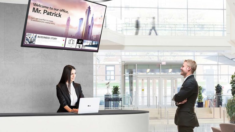 LG TV screen mounted on wall behind receptionist and a man watching LG TV