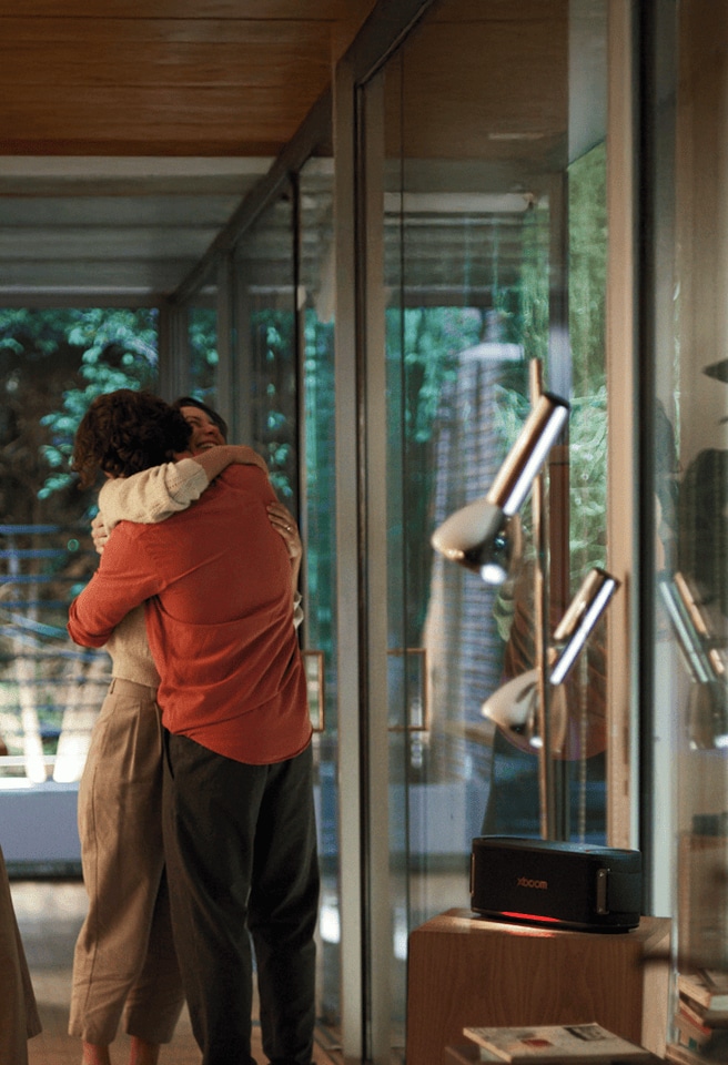 A woman and a man embrace in the living room, with the LG xboom speaker turned on beside them.