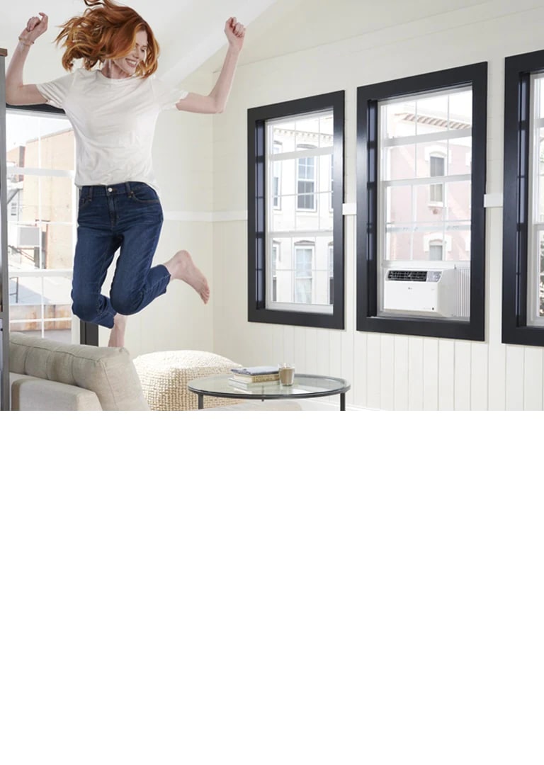 LG window air Conditioner in a living room and a woman jumping on a sofa