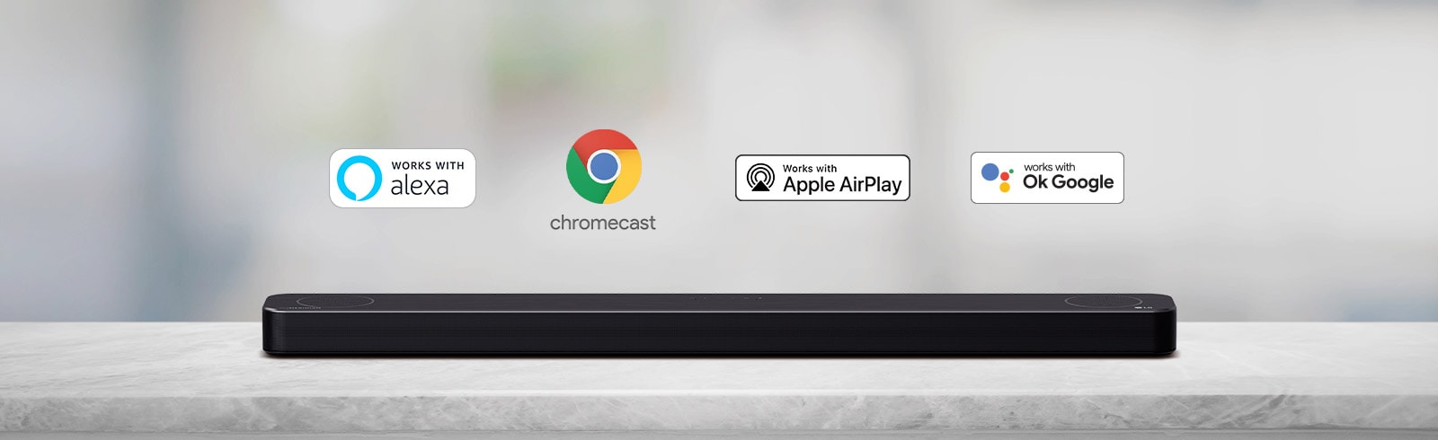 There is a soundbar placed on a gray shelf and there are AI platform logos, in order of Alexa, Chromecast, Apple Airplay, and OK Google from left to right.
