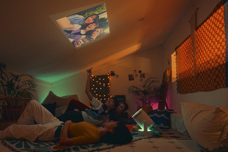 Friends lay on the bedroom floor watching a projection on the ceiling. 