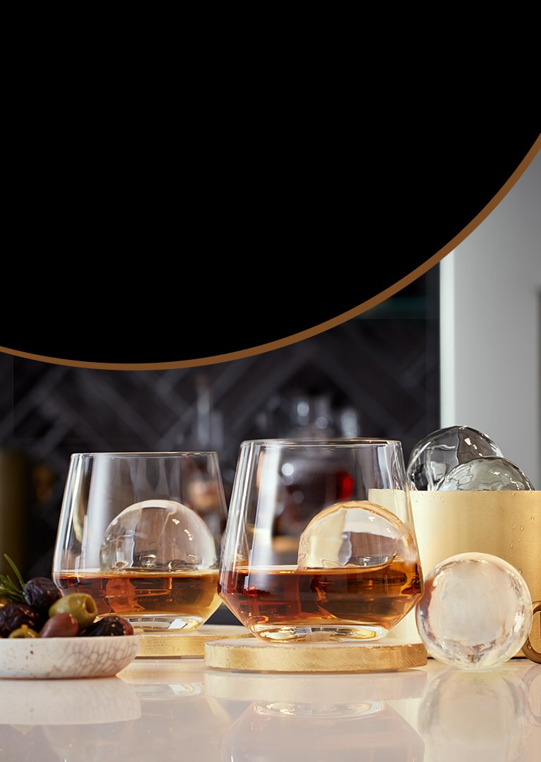 Alcoholic tumbler glasses on a table surrounded by ice and fruit.