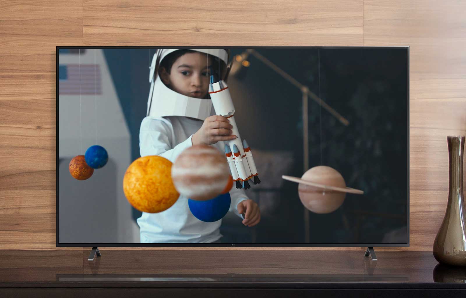 A TV screen playing a video of a boy in an astronaut suit he made playing with a spaceship in his room decorated with miniatures of planets (play the video)