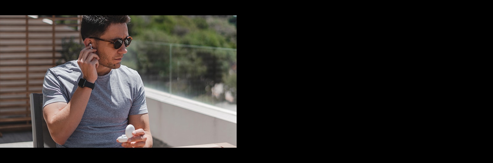 An image of a man with sunglasses taking out the earbud with automatic ear detection on a balcony