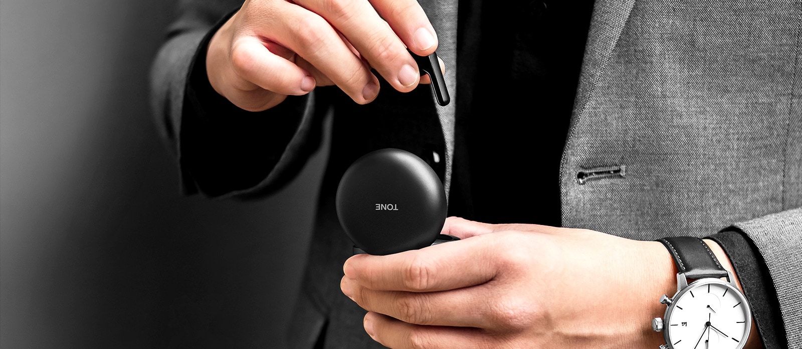 An image of a man dressed in grey suit holding a black LG TONE Free Fn6 cradle and taking out an earbud from it