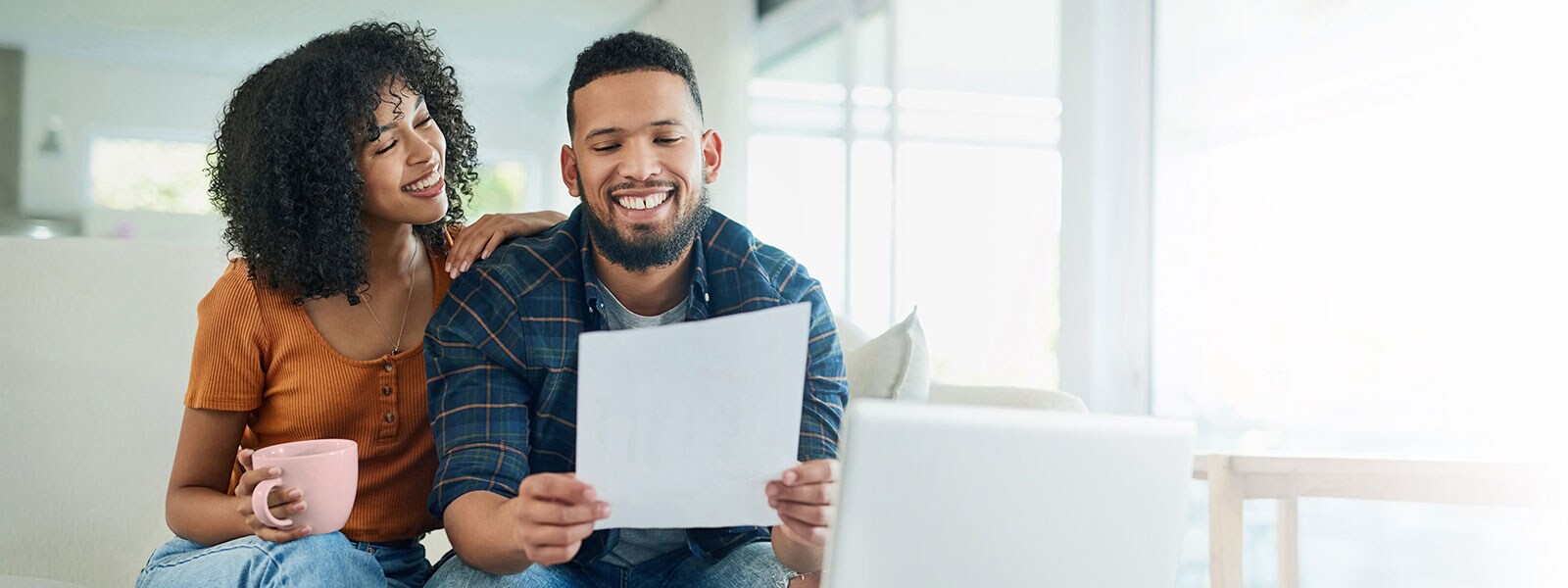 a woman holding a coffee mug and a man reading the energy bill on their couch