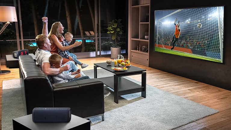 A family sitting on a couch watching soccer on TV with sound connected on LG Xboom Speakers making QNED the best tv for sports 